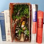 A forest book nook with twigs and flowers and a gnome nestled in between old books.