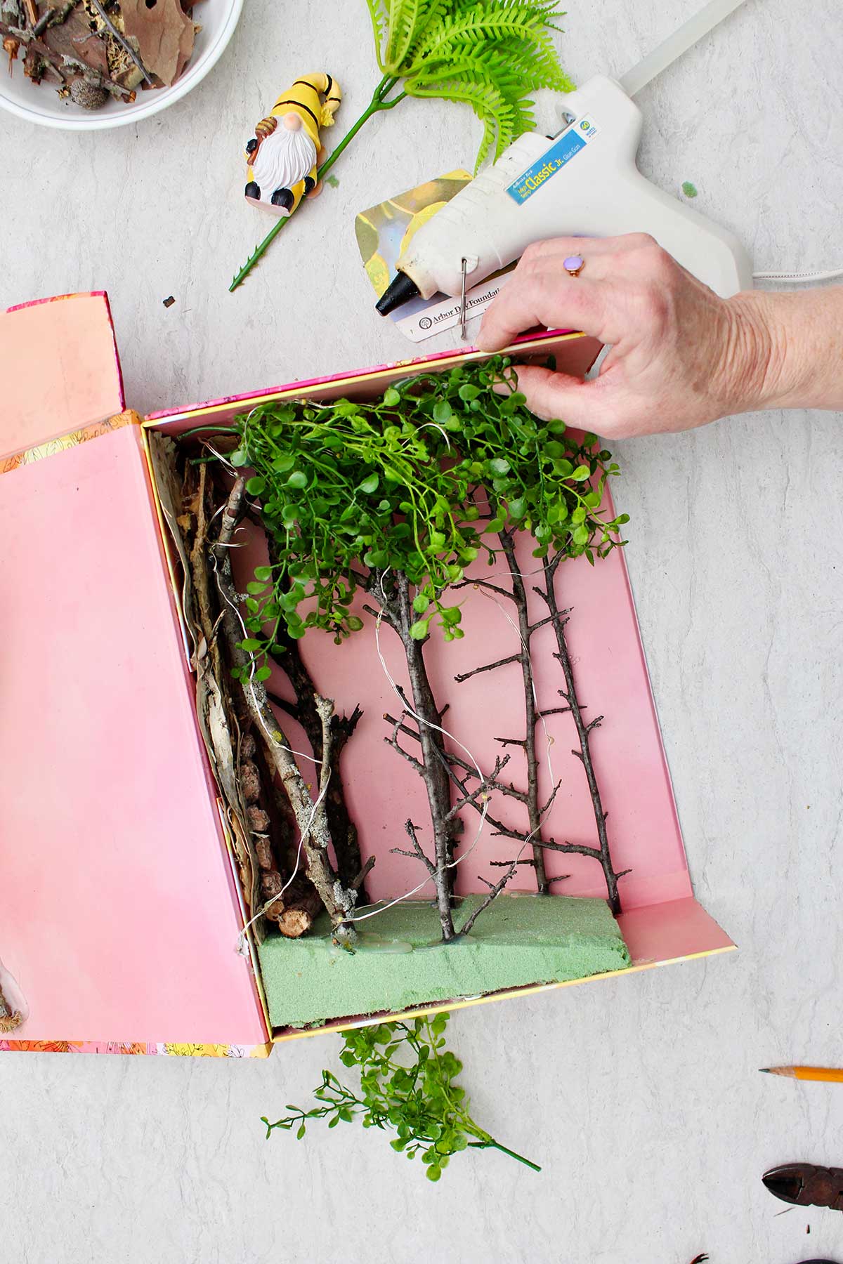 A person hot gluing fake foliage to the top of the book nook shelf insert.