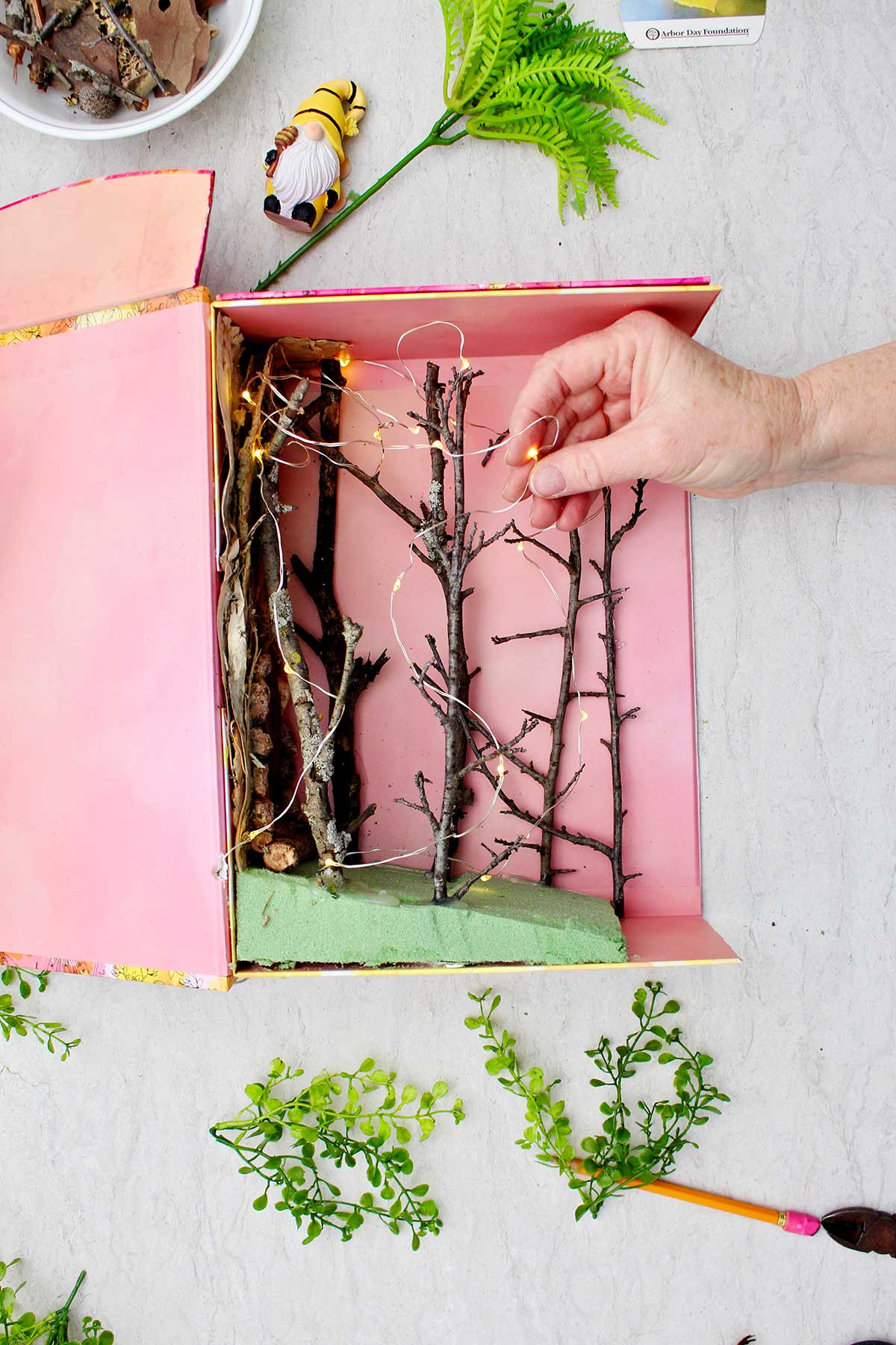 A person placing fairy lights around the twigs inside the book nook shelf insert.