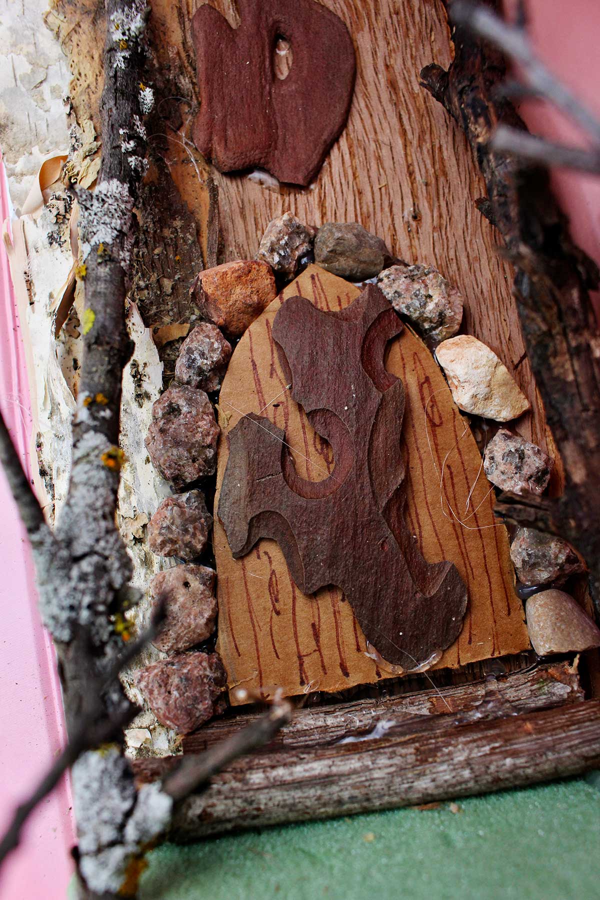 Close up view of a rounded door made to look like tree bark with small rocks around it.