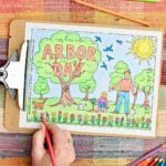 A person coloring in flowers pink on the Arbor Day coloring page which is in a clip board resting on a plaid placemat surrounded by colored pencils.