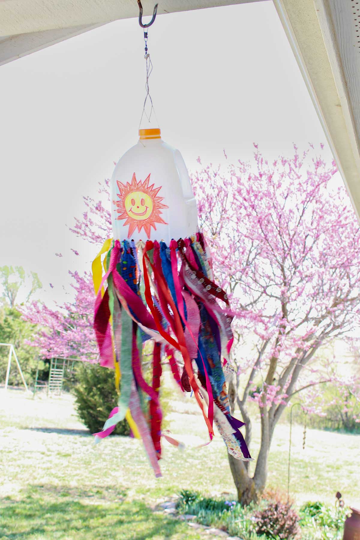 A milk jug windsock blowing in the breeze with a purple flowered tree behind it.