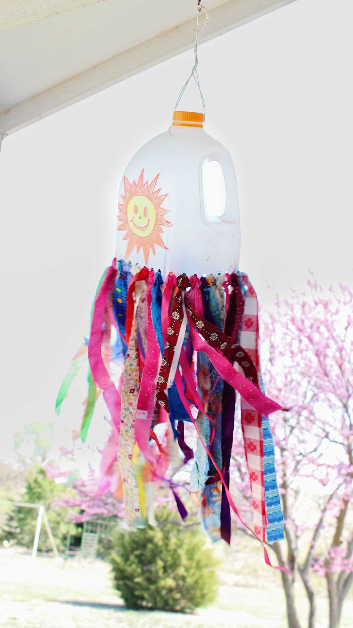 A milk jug windsock blowing in the breeze with a purple flowered tree behind it.