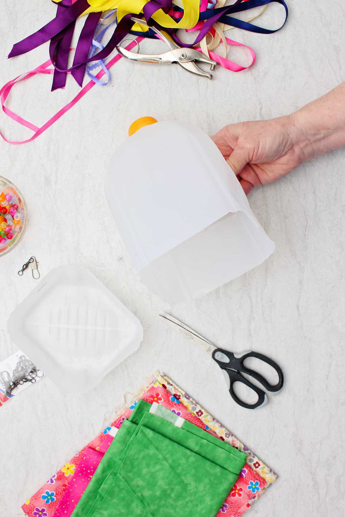 Person showing the cut off bottom of an empty milk jug with other supplies near by.