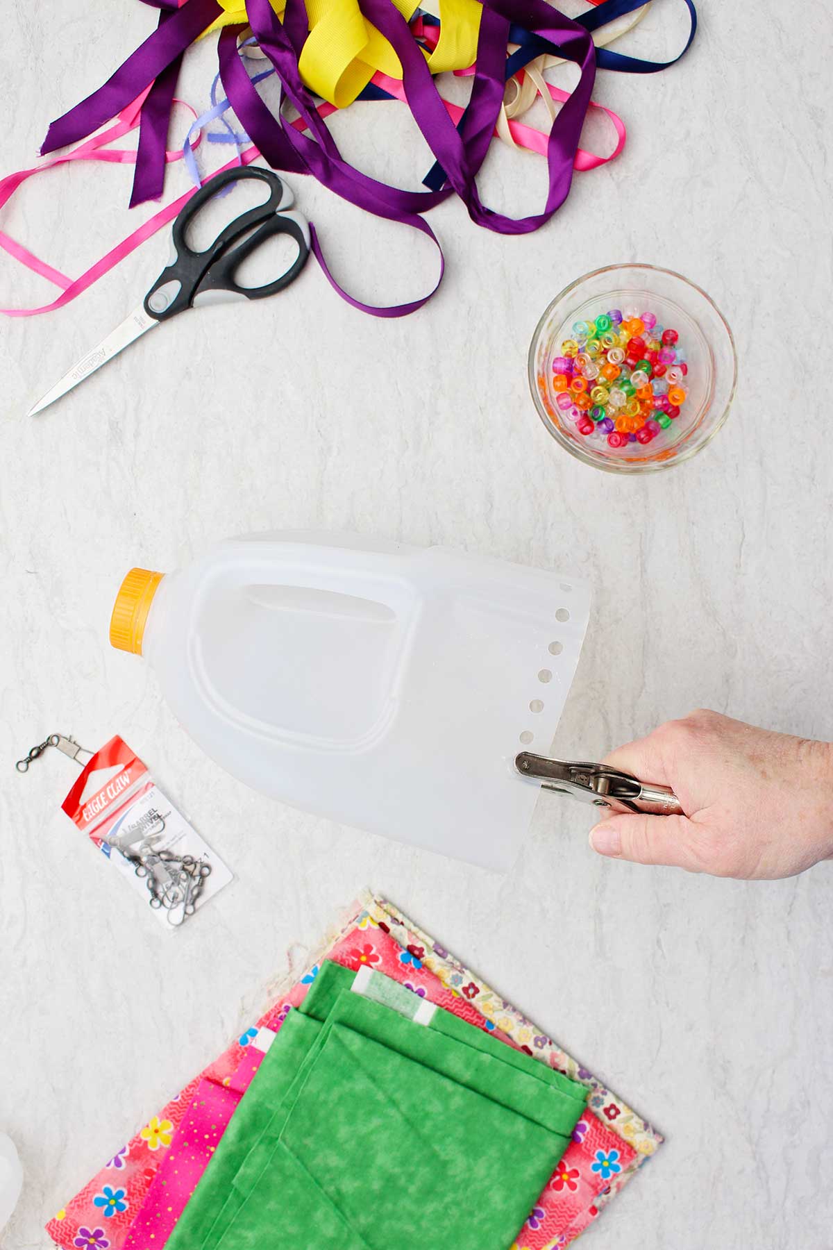 Person punching holes into the bottom of a cut off empty milk jug with other supplies near by.