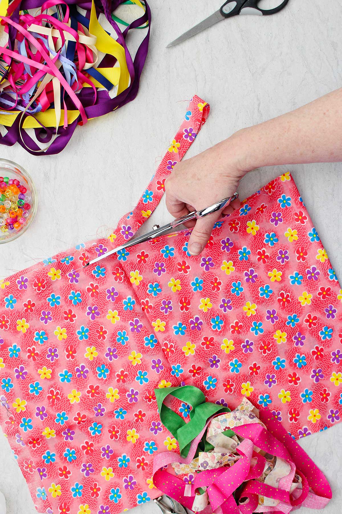 Person cutting strips of bright flowered fabric with other fabric pieces and ribbon near by.