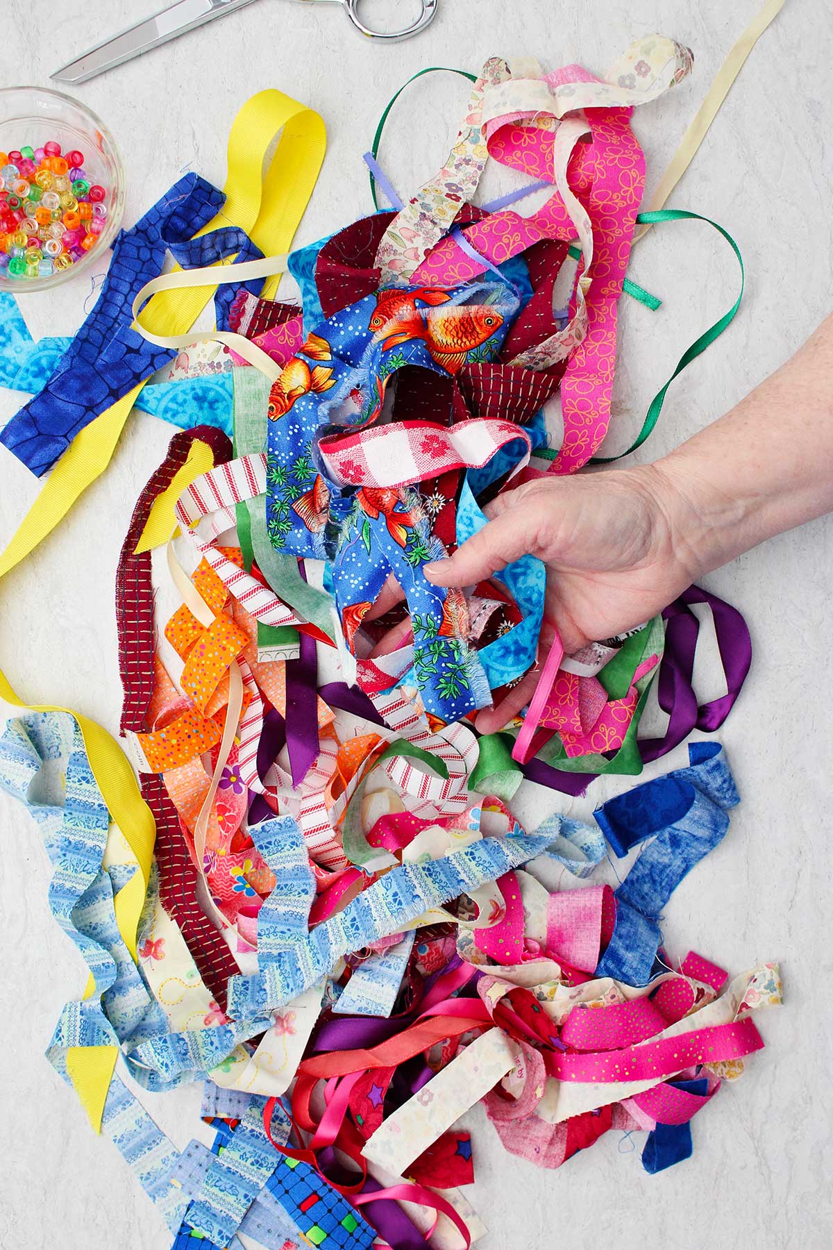 Person holding and displaying a large pile of colorful strips of fabric scraps.