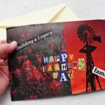 Person showing a Father's Day card with red flowers and a windmill against a sunset with type saying "Happy Father's Day"