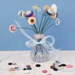 A salt shaker full of button flowers with a ribbon tied around it against a blue background.