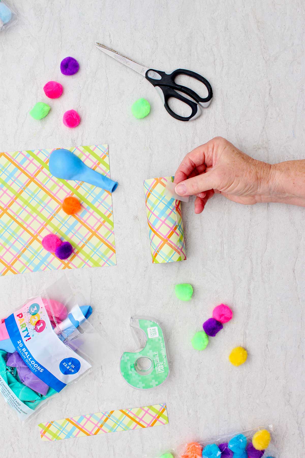 Person taping plaid patterned paper around a toilet paper tube to make into a marshmallow launder.