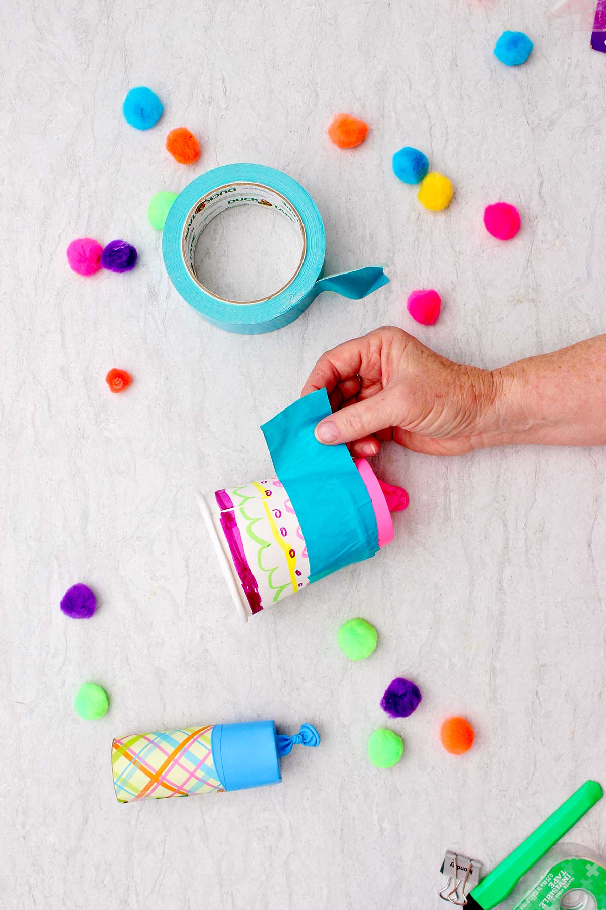 Person securing balloon to the paper cup with a large piece of blue duct tape.