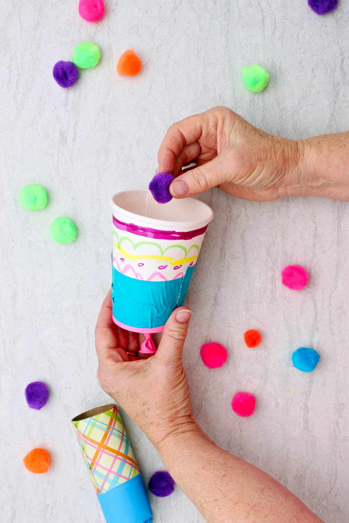 Person placing a purple pom pom into a decorated marshmallow shooter.