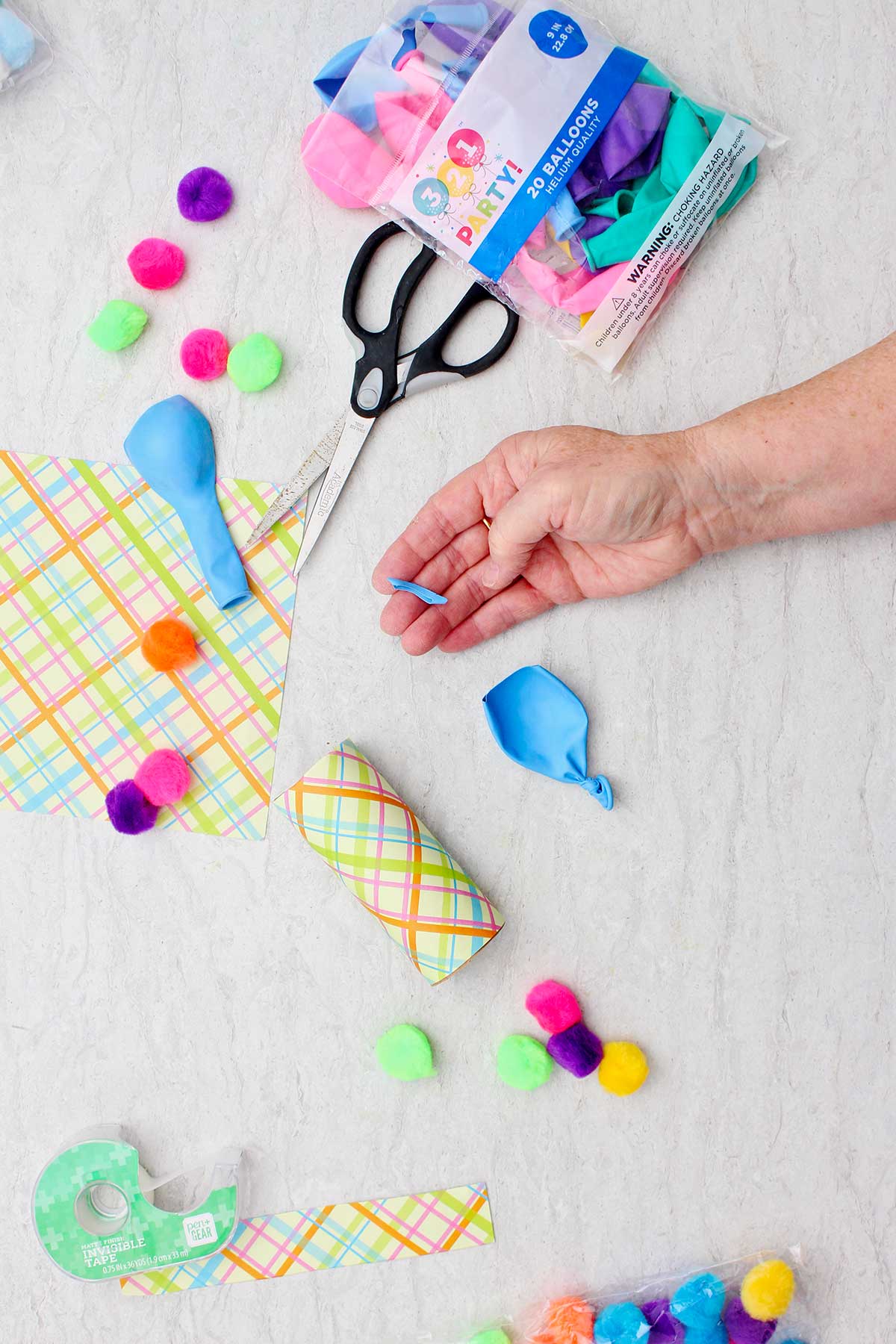Person showing the cut blue balloon that will be attached to the marshmallow shooter with supplies near by.