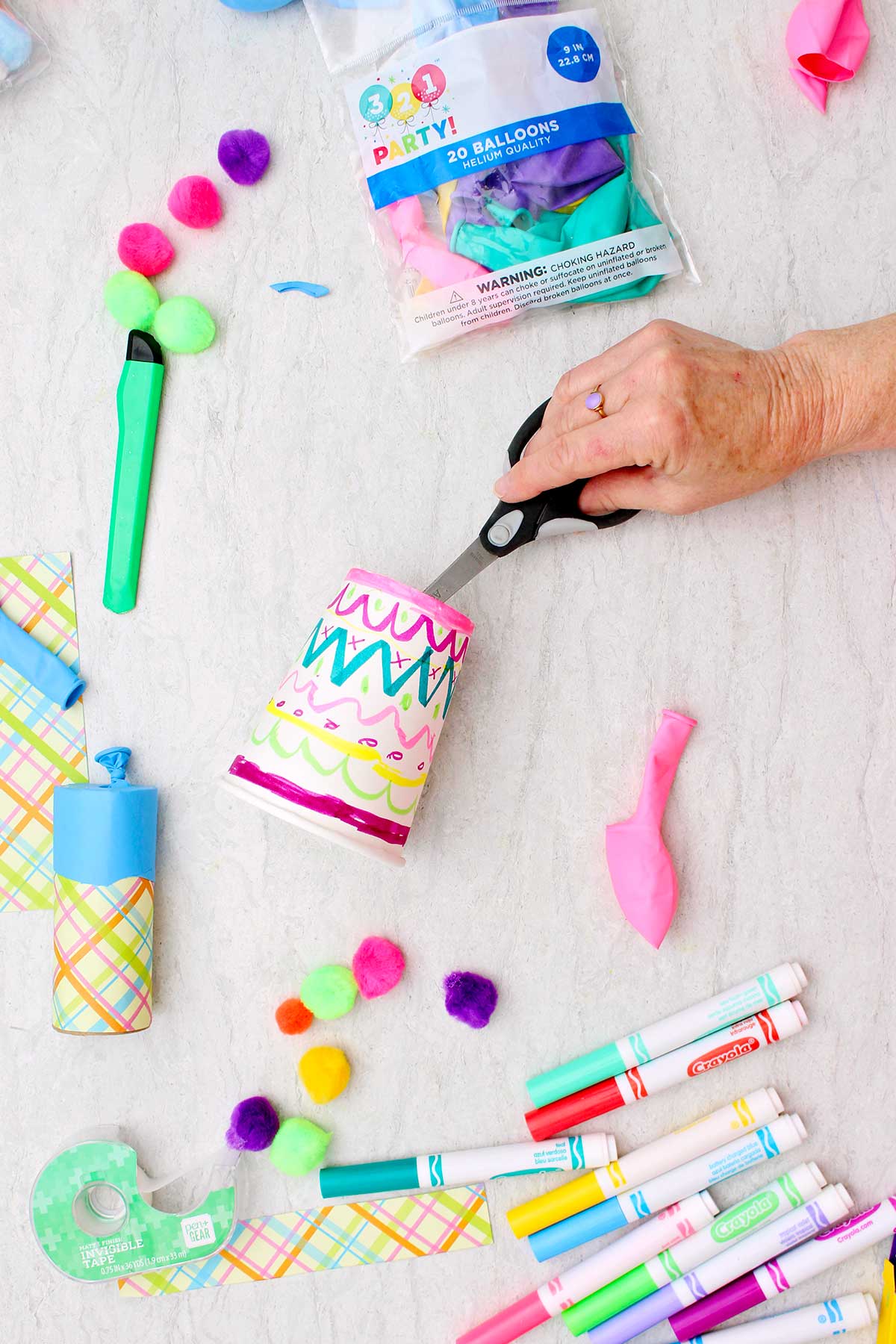 Person cutting out the bottom of a decorated paper cup with supplies near by.