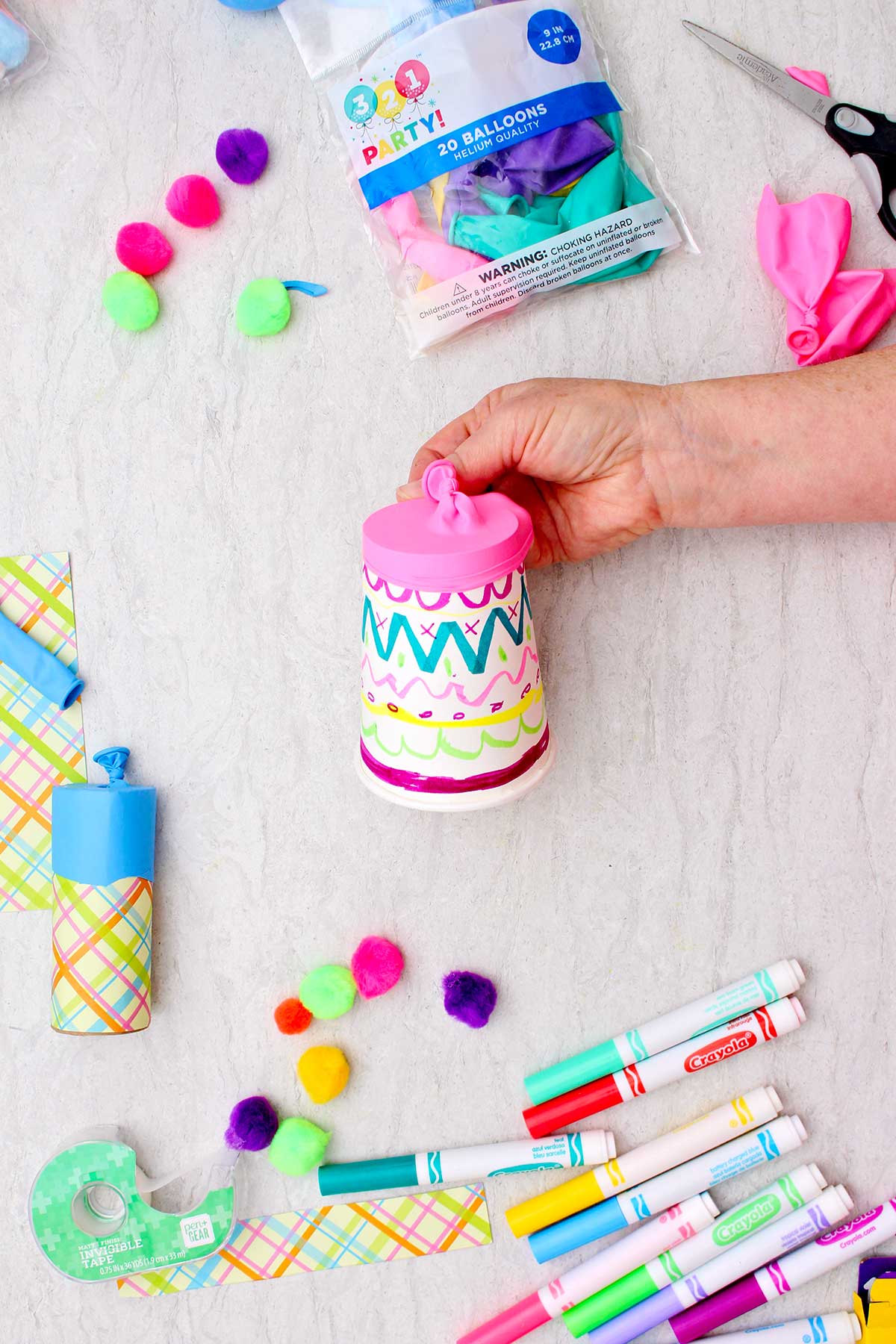 Person showing a decorated paper cup with pink cut balloon on the end.