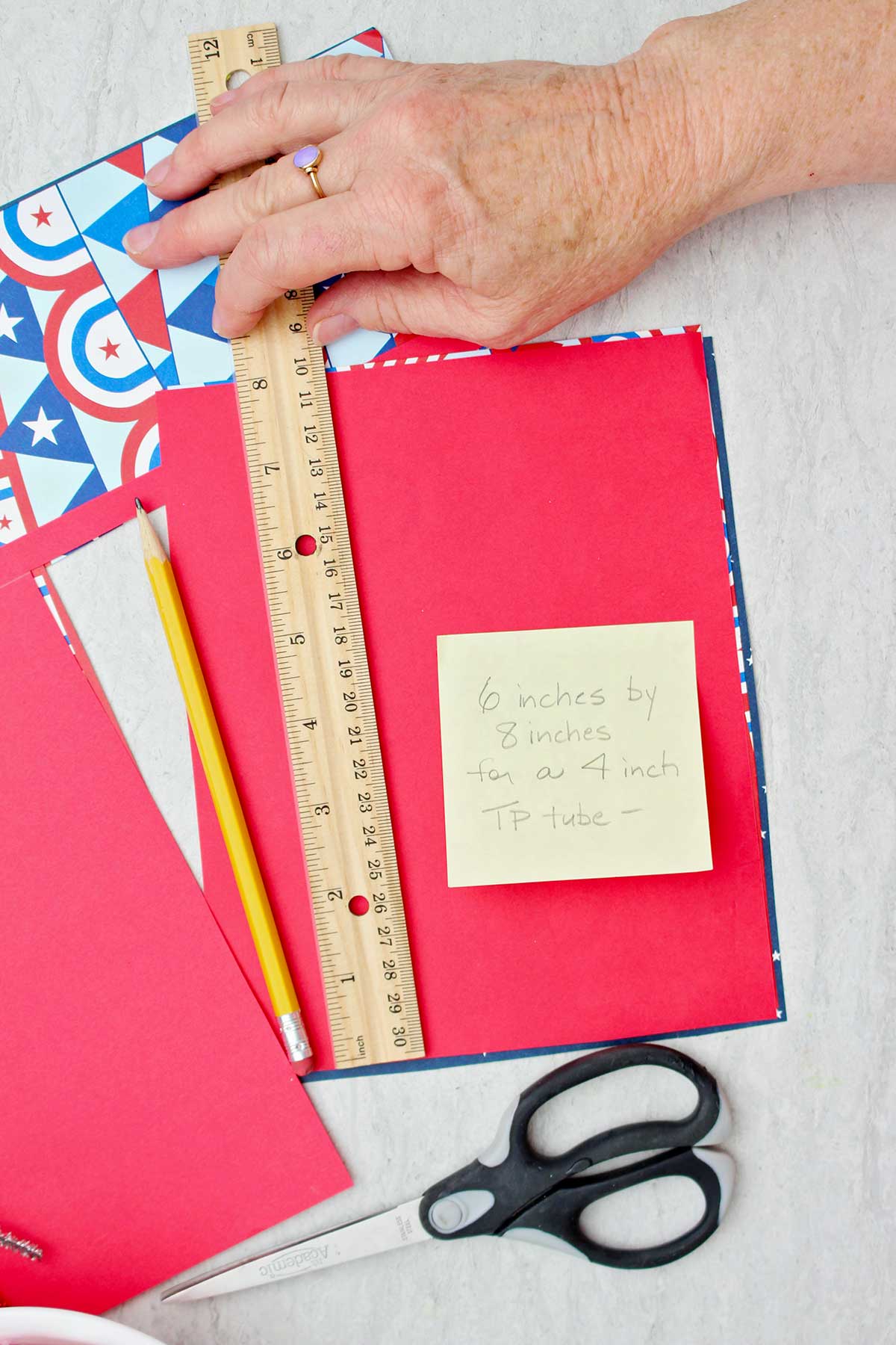 Person measuring scrapbook paper to fit around a toilet paper tube.
