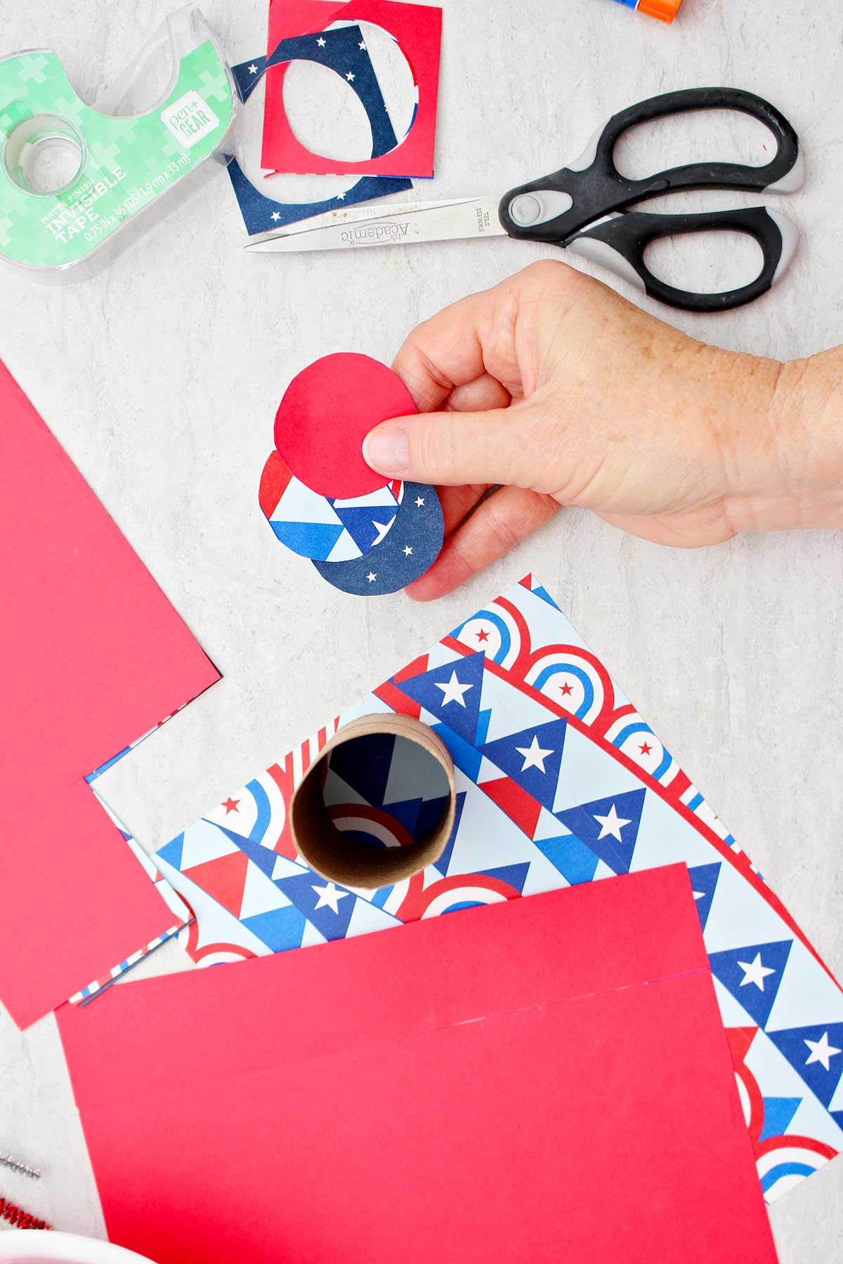 Person holding three circular cut outs of scrapbook paper that will be used to close the bottom end of a firecracker treat box.