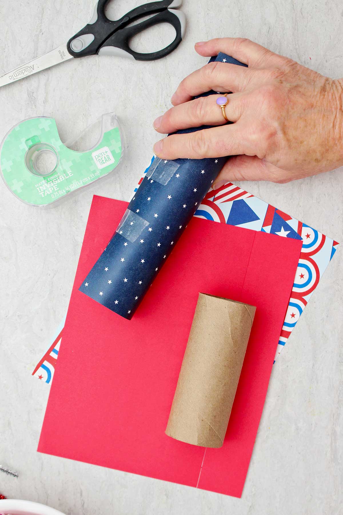 Person holding a toilet paper tube wrapped in blue star patterned scrapbook paper and taped.