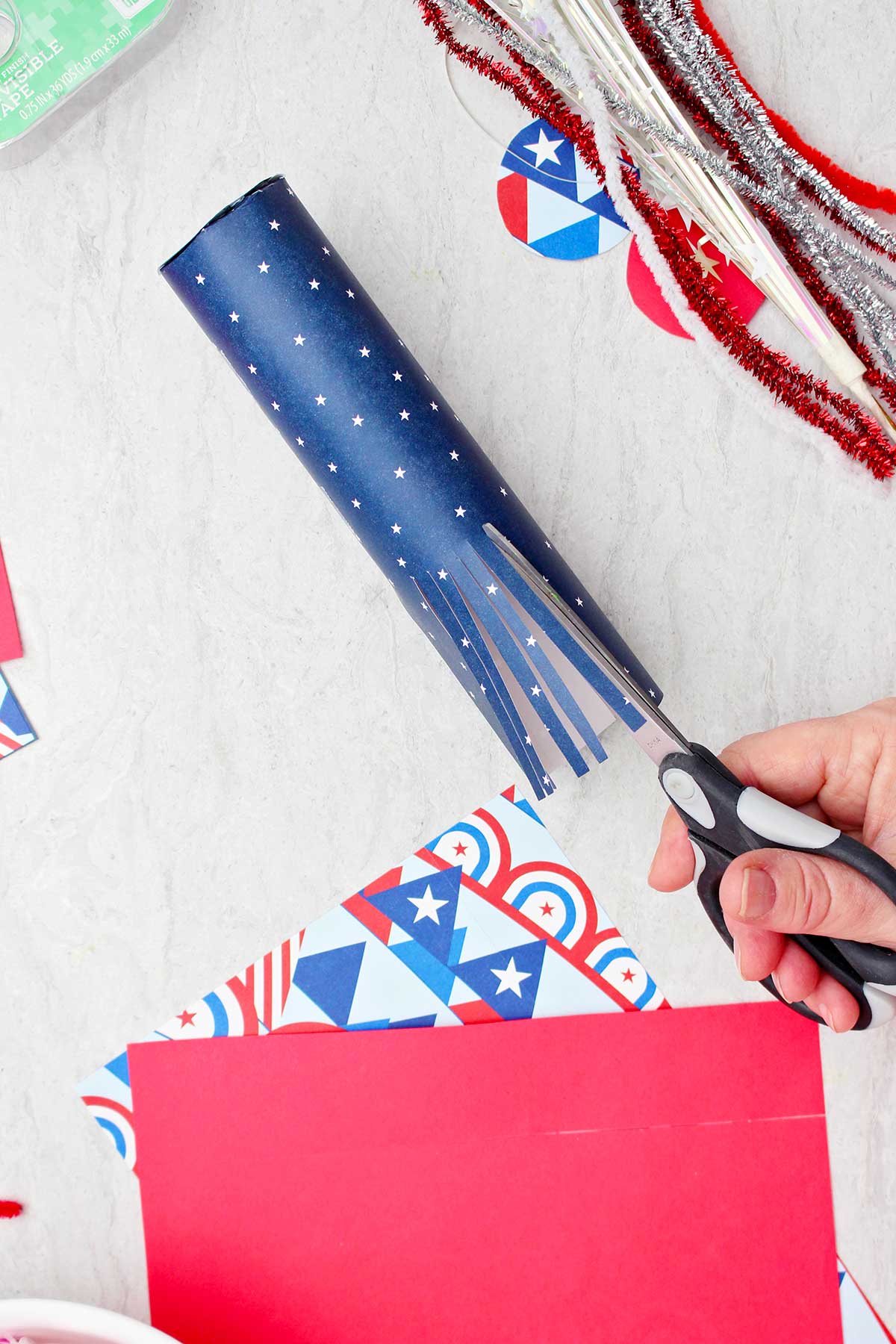 Person cutting scrapbook paper wrapped around a toilet paper tube to look like fringe.