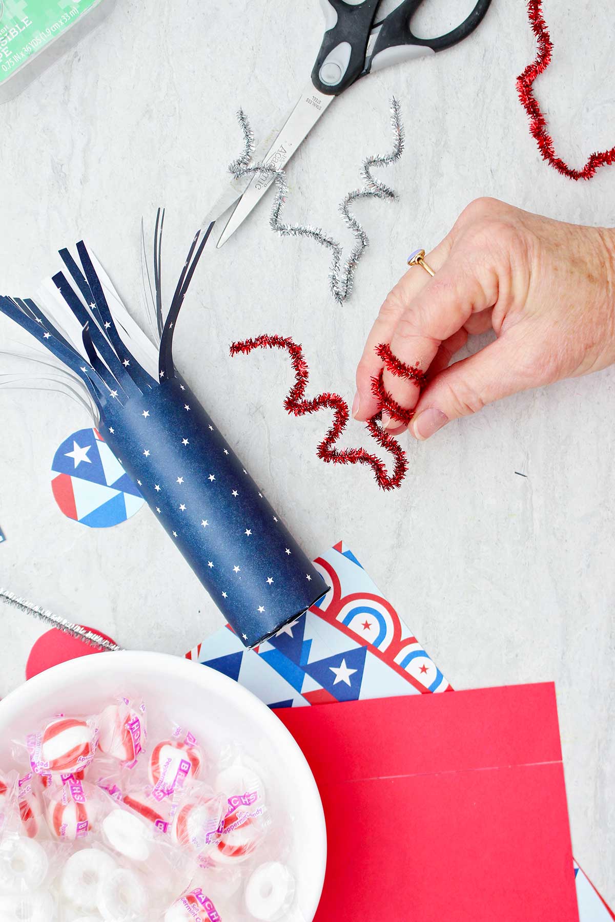 Person bending red sparkly pipe cleaner around finger to make it twirly.