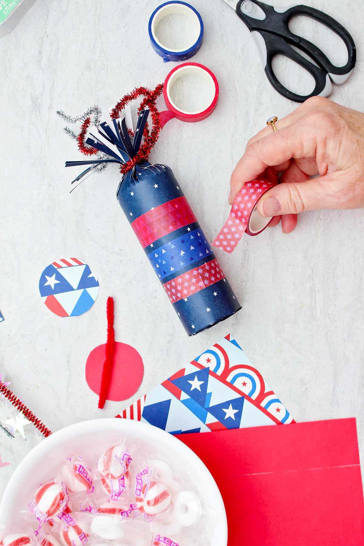 Person decorating blue firecracker treat box with red patterned washi tape.