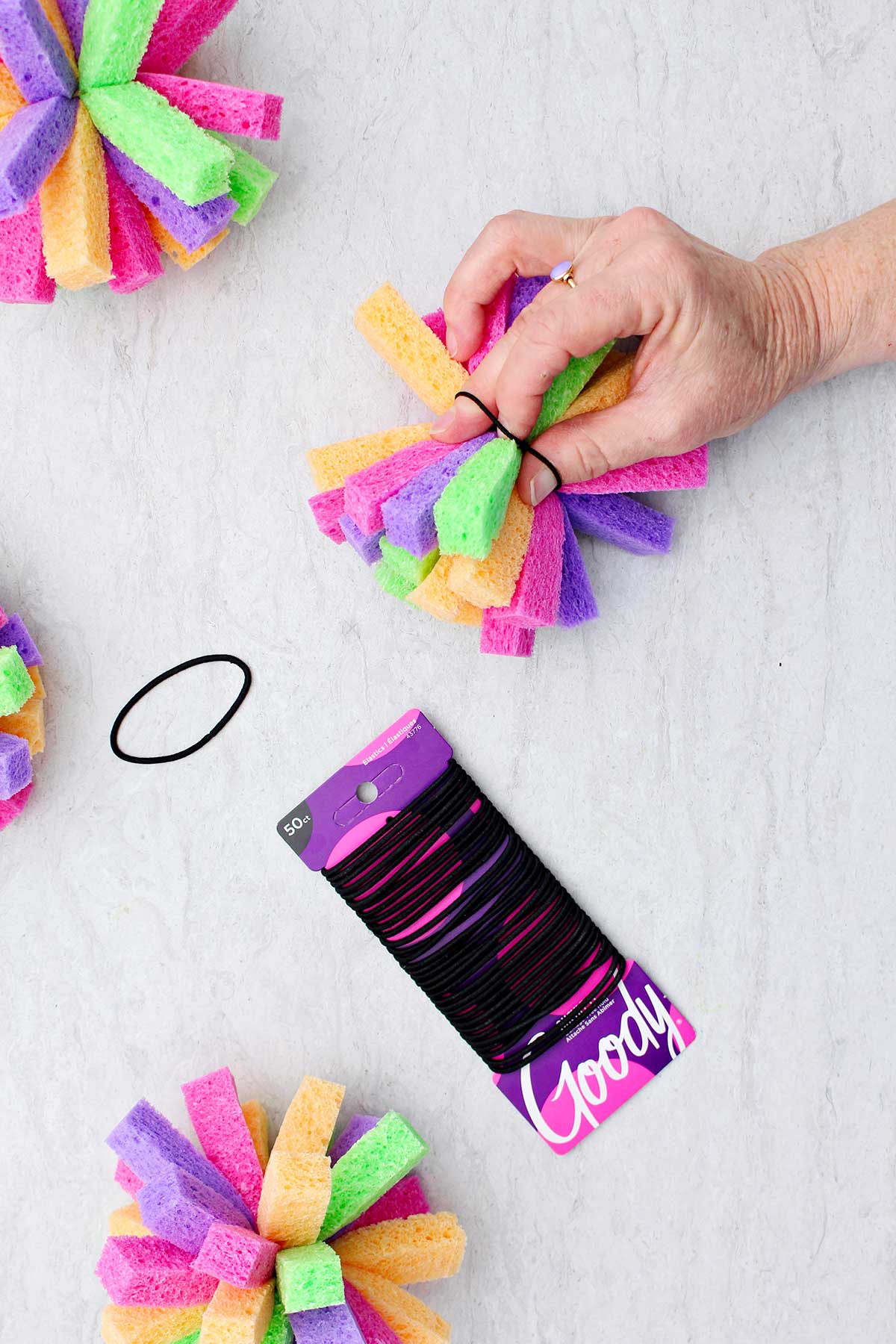 Person using small black hair ties to secure sponge pieces together.