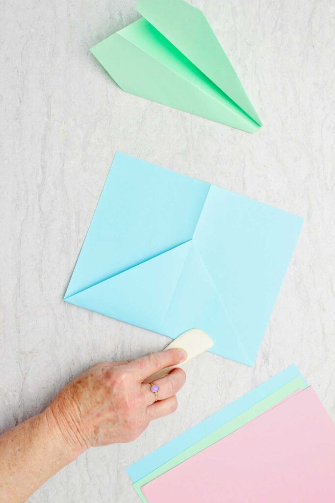 Person using a wooden bone folder to fold a blue piece of paper looking somewhat like an envelope.