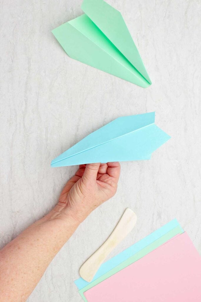 Person holding a blue paper airplane with a green plane and paper near by.
