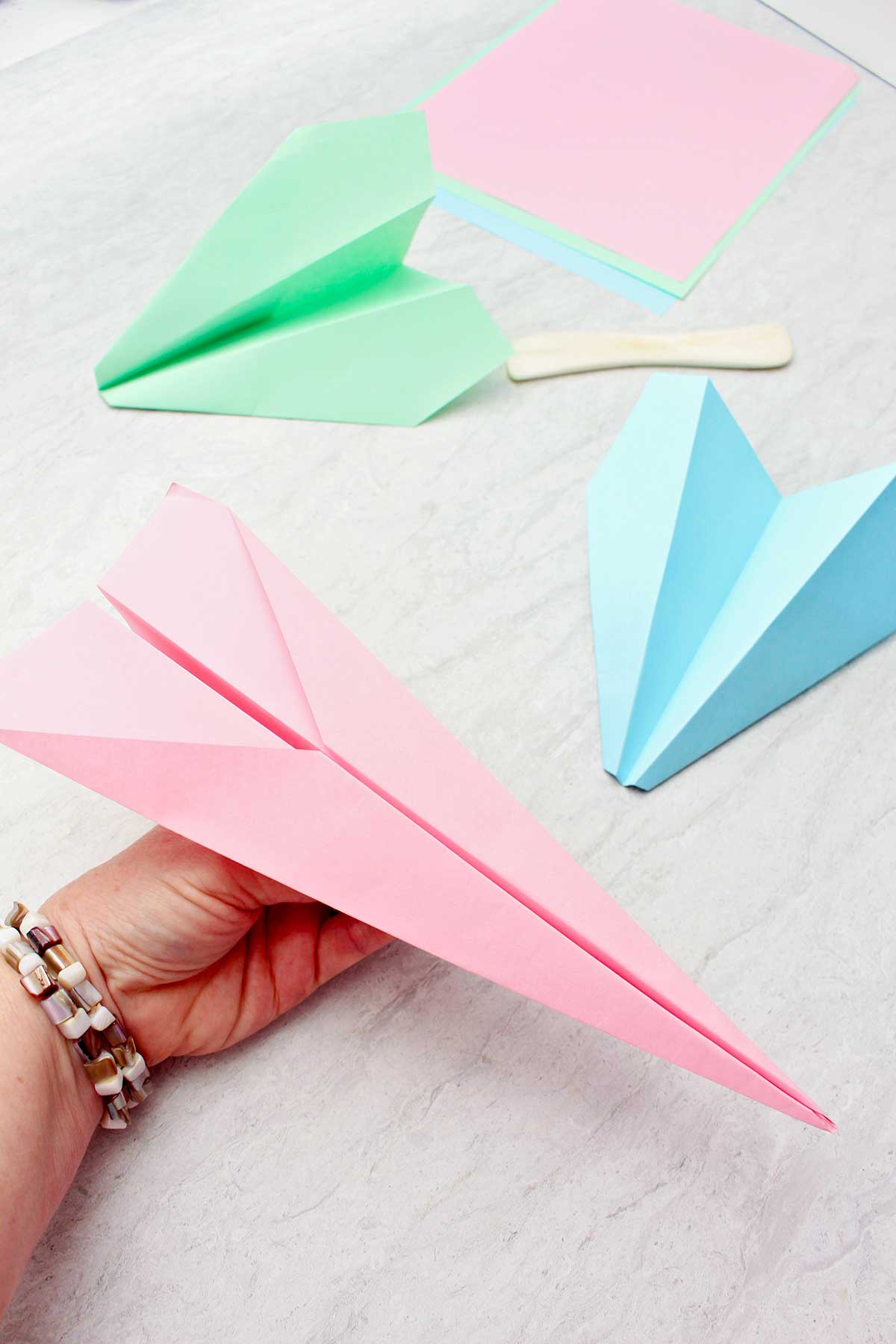 Person holding a light pink paper airplane with two other paper airplanes near by.
