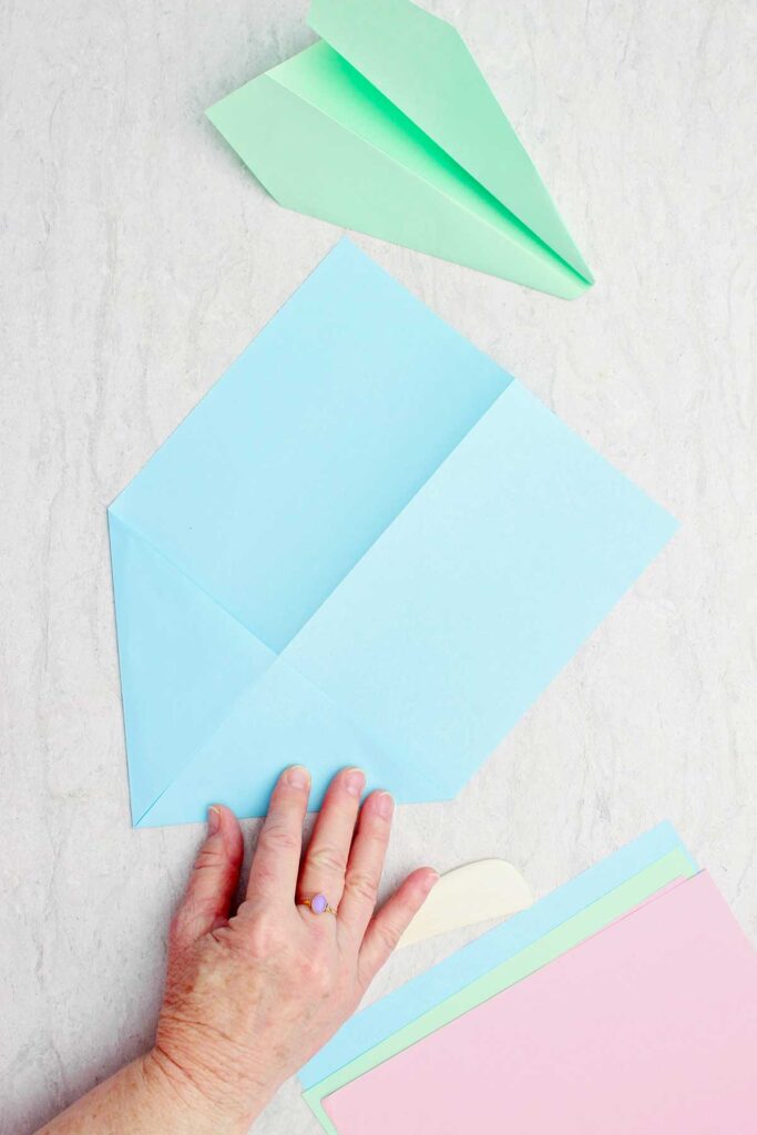 Person folding top portion of paper airplane in blue paper.