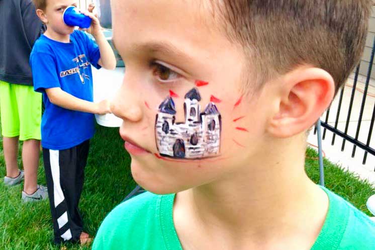 Young boy outside with green shirt with castle face painting.