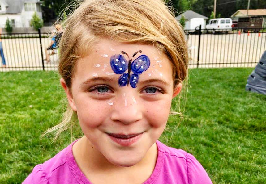 Young girl outside in purple shirt with blue butterfly face painting.