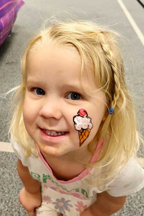 Young girl with blonde hair with ice cream cone face painting.