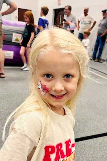 Young girl with blonde hair with unicorn face painting.