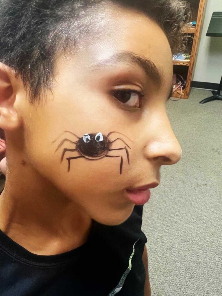 Young boy in a black shirt with a black spider face painting.