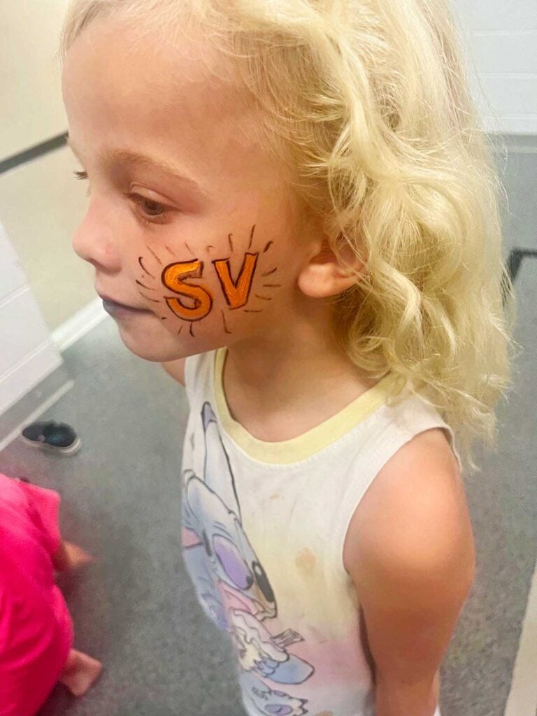 Young girl with blonde hair with orange "SV" face painting.