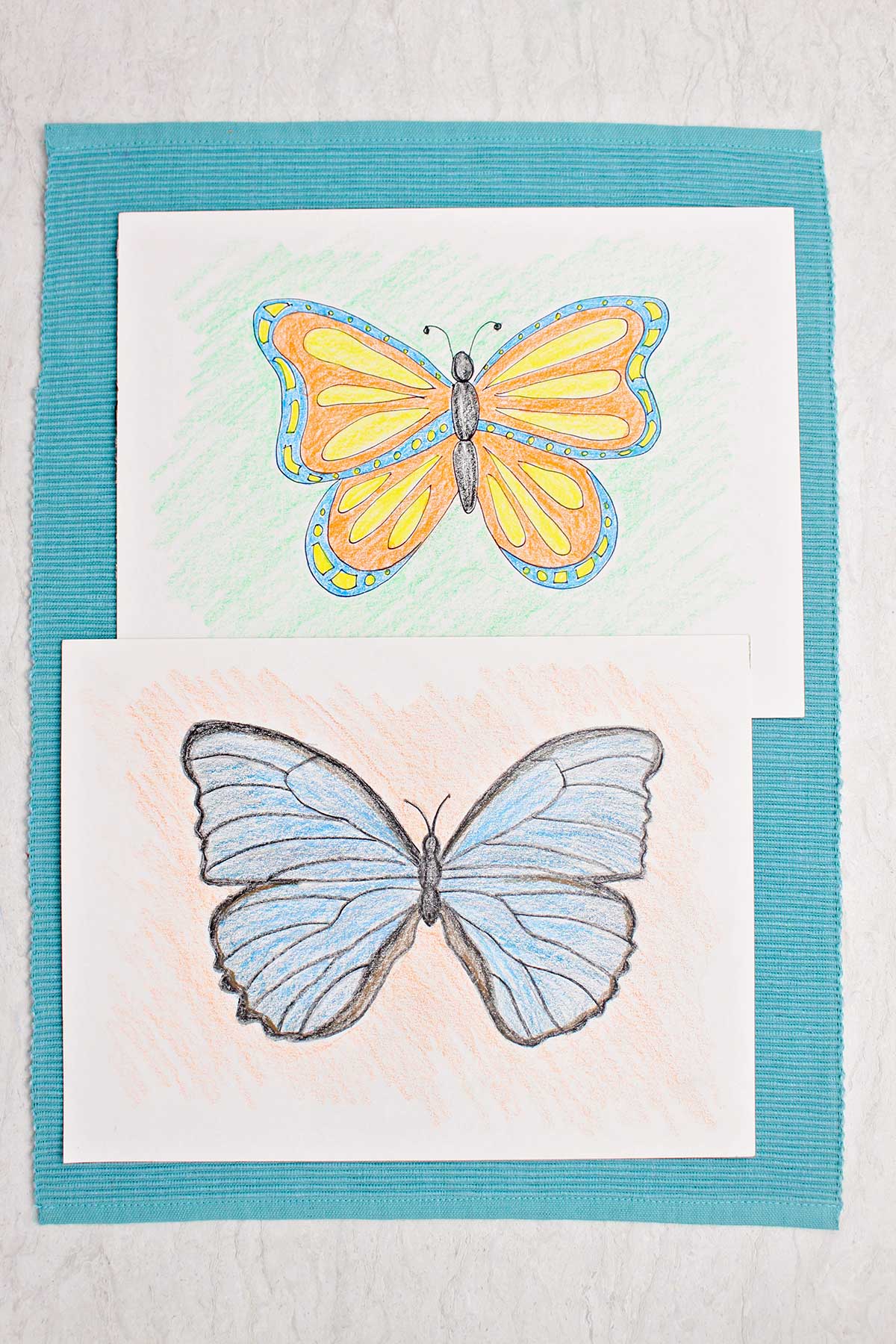 Blue and black colored butterfly drawing and orange, yellow and blue colored butterfly on blue placemat.