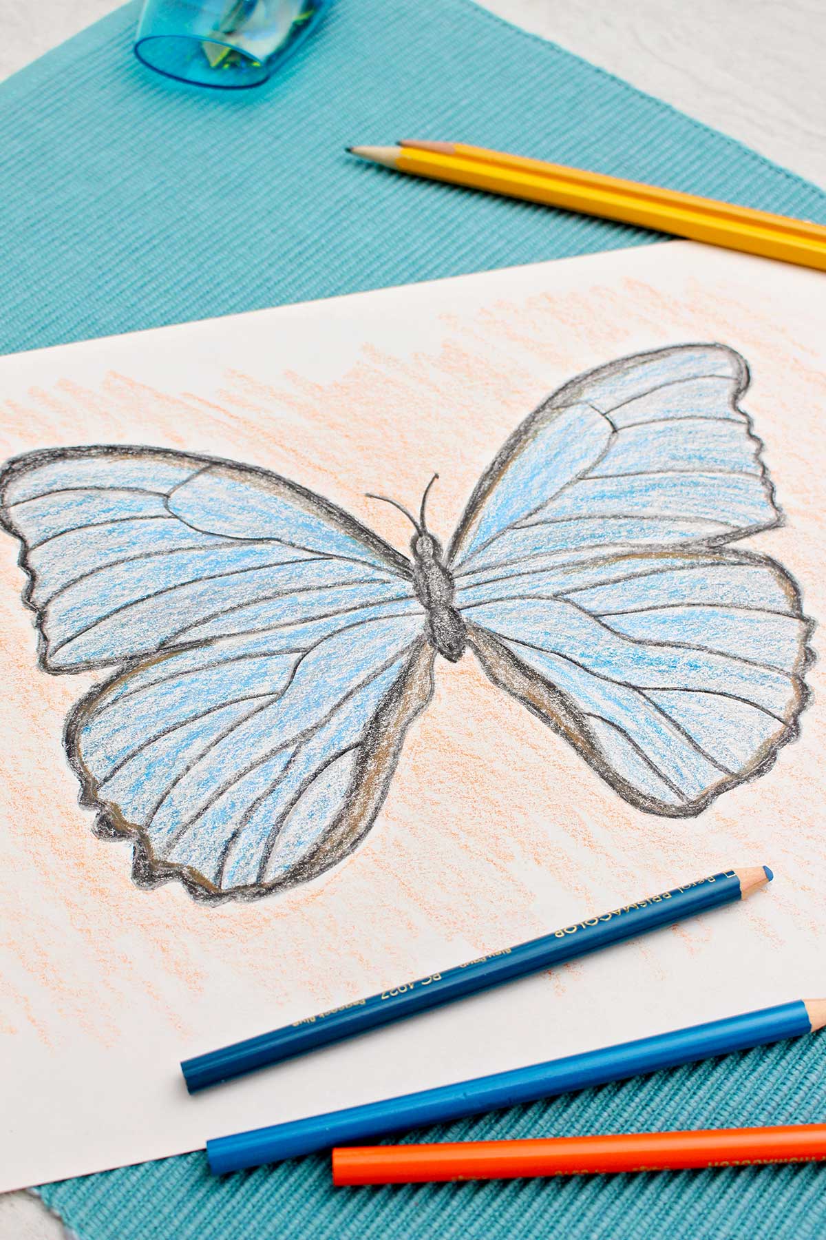 Blue and black colored butterfly drawing on blue placemat with colored pencils and sharpies around.