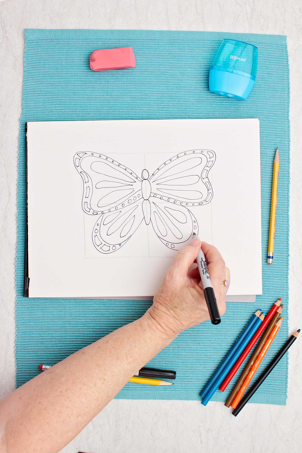 Person going over pencil in sharpie to make butterfly drawing pop!