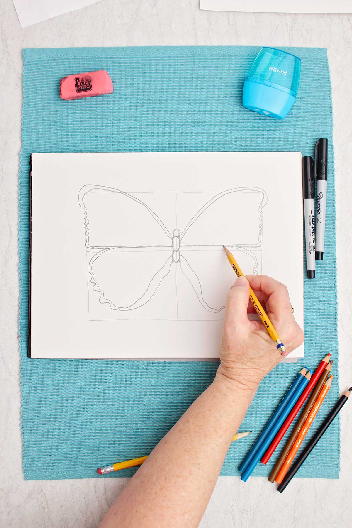 Person sketching the four quadrants of a butterfly drawing.