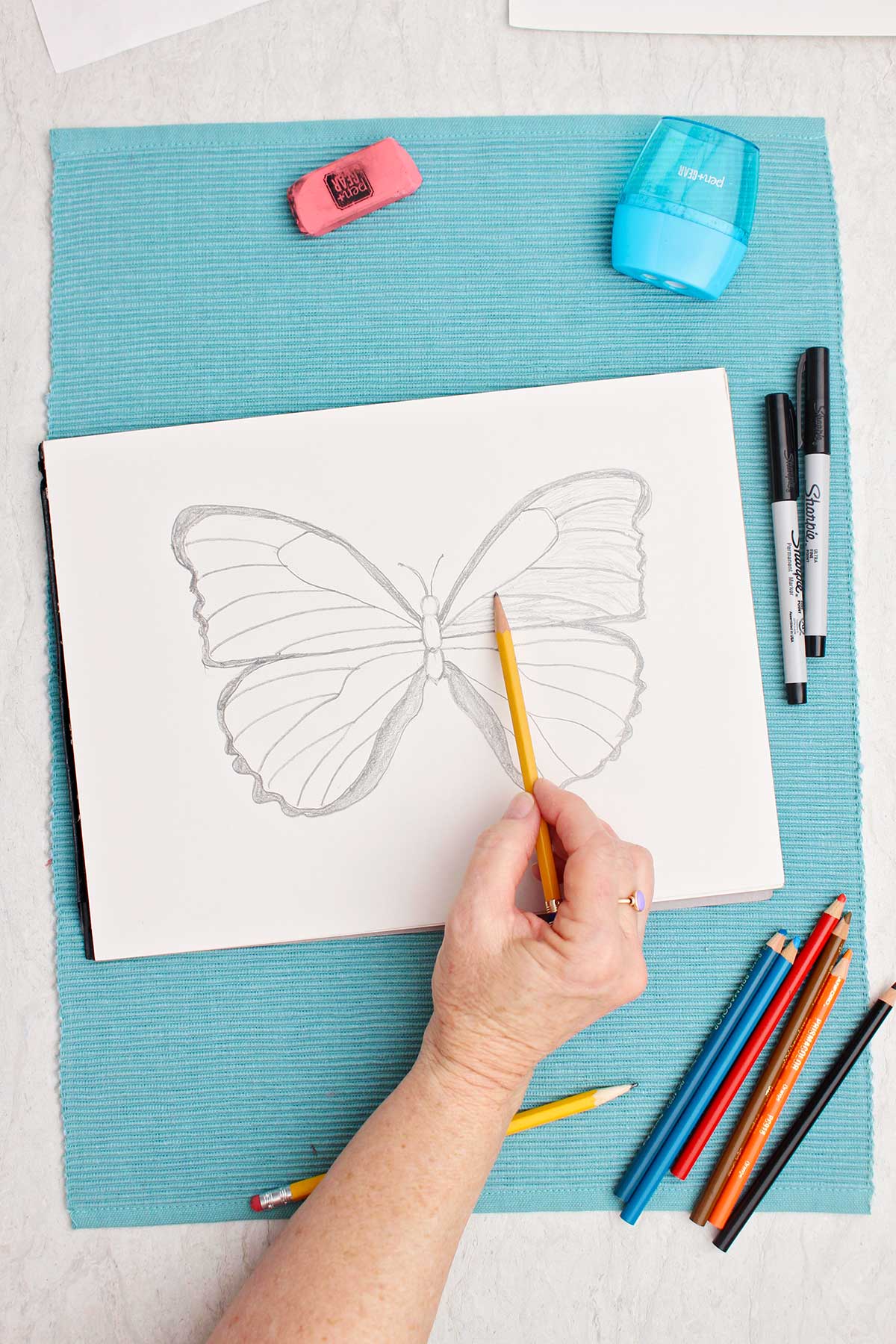 Person gently coloring in wings on butterfly drawing with side of pencil.