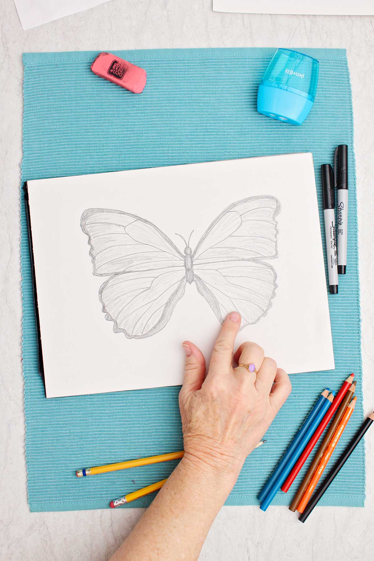 Person using their finger to smooth and shade the pencil marks made on butterfly drawing.