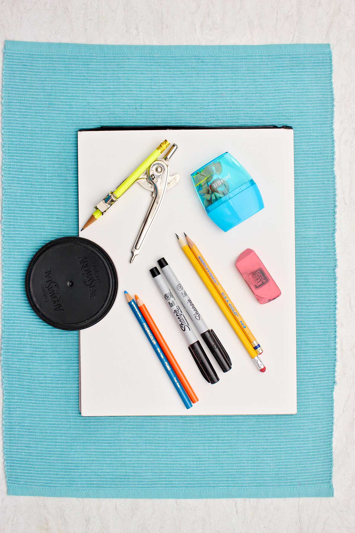 A coffee lid for tracing, sharpies, pencils, eraser, colored pencils, compass and pencil sharpener.