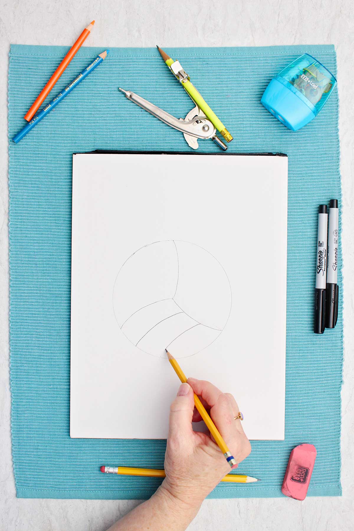 Person sketching detail lines on volleyball drawing with pencil.