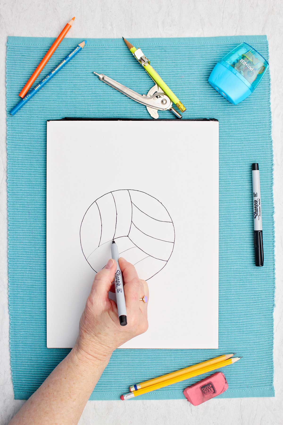 A person tracing over pencil lines with a sharpie on volleyball drawing.
