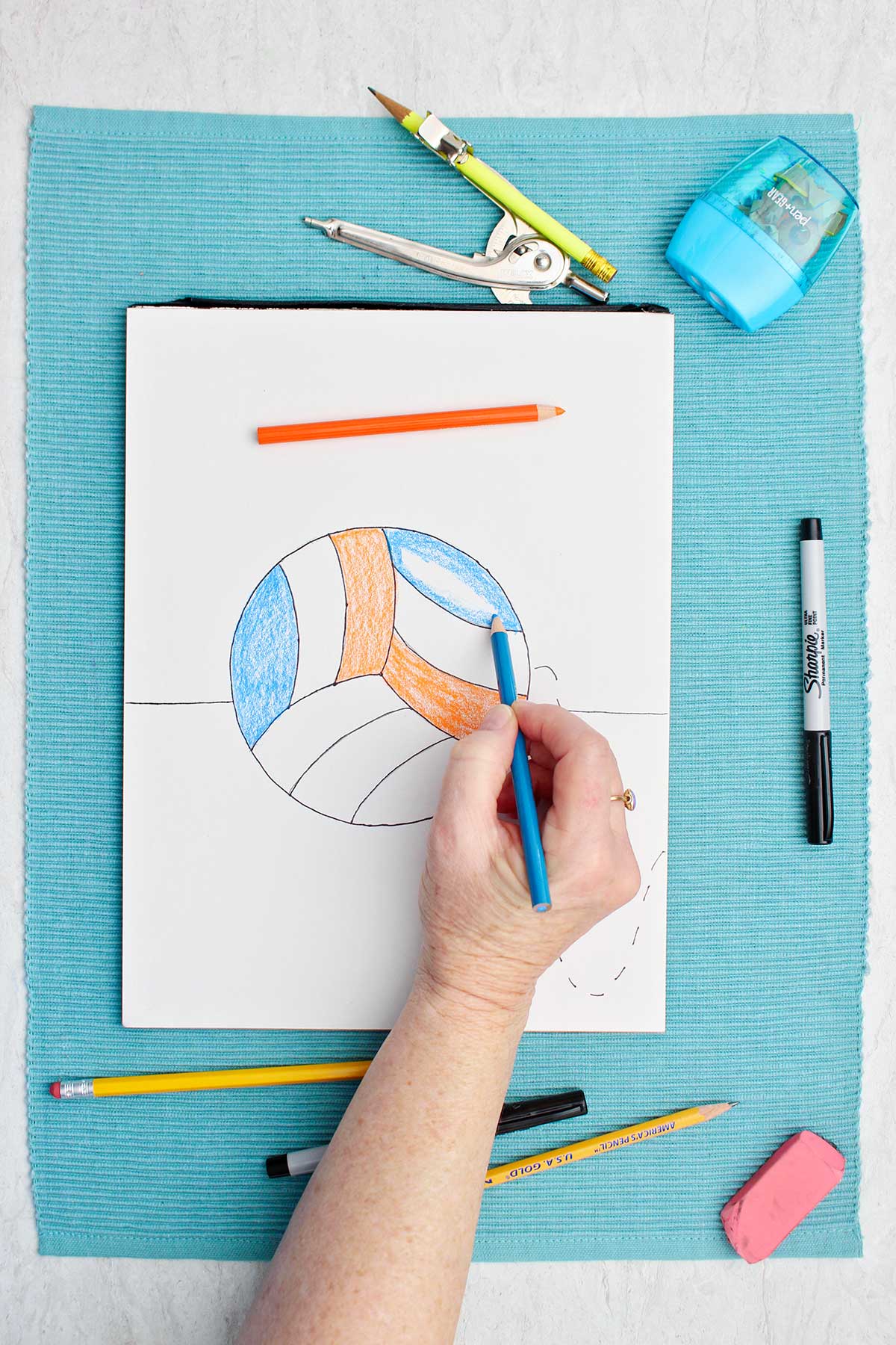 Person coloring in a sketch of a volleyball with blue colored pencil.