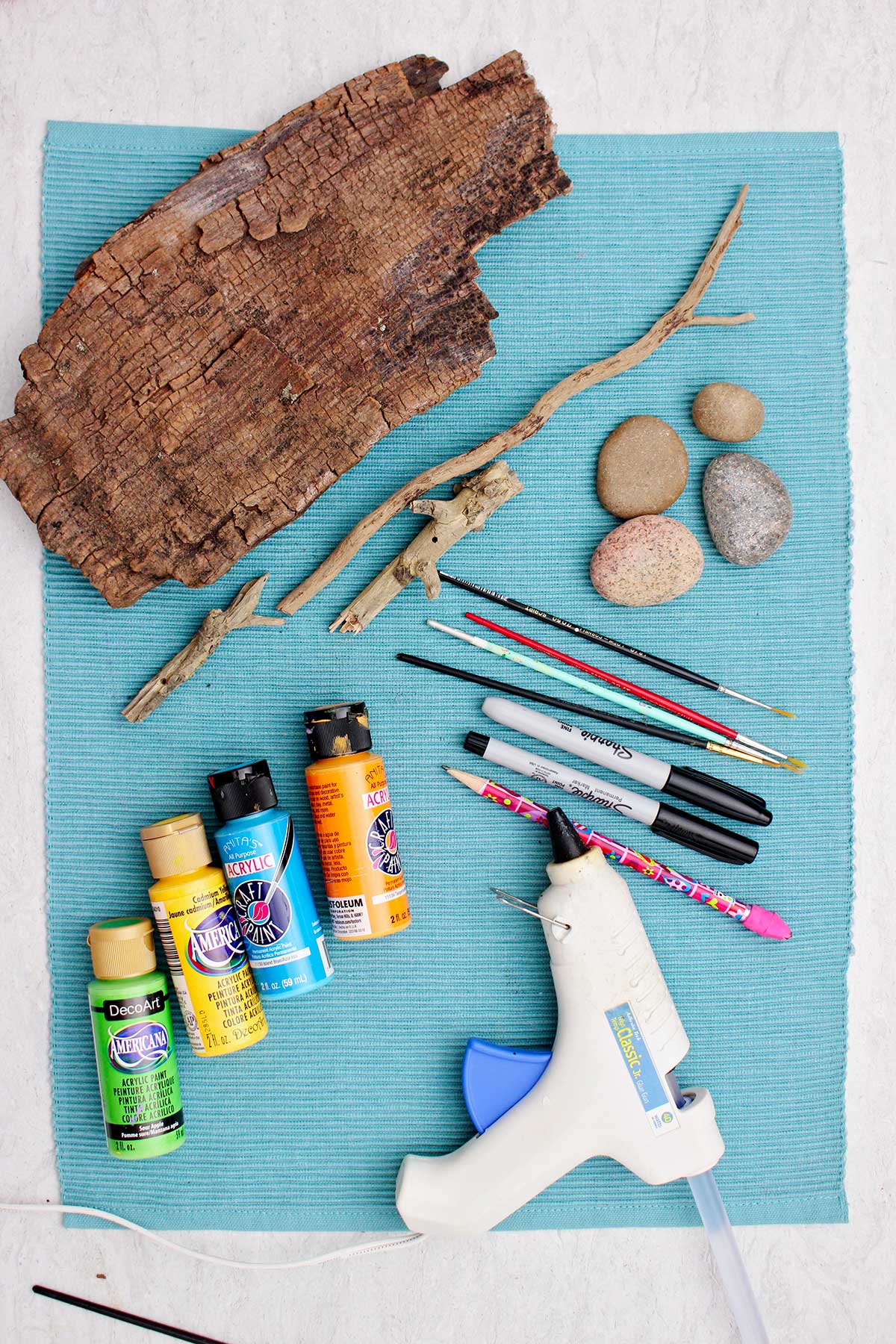 Smooth rocks, paintbrushes, sharpie markers, paint, glue gun and wood pieces to make owl painted rock artwork.