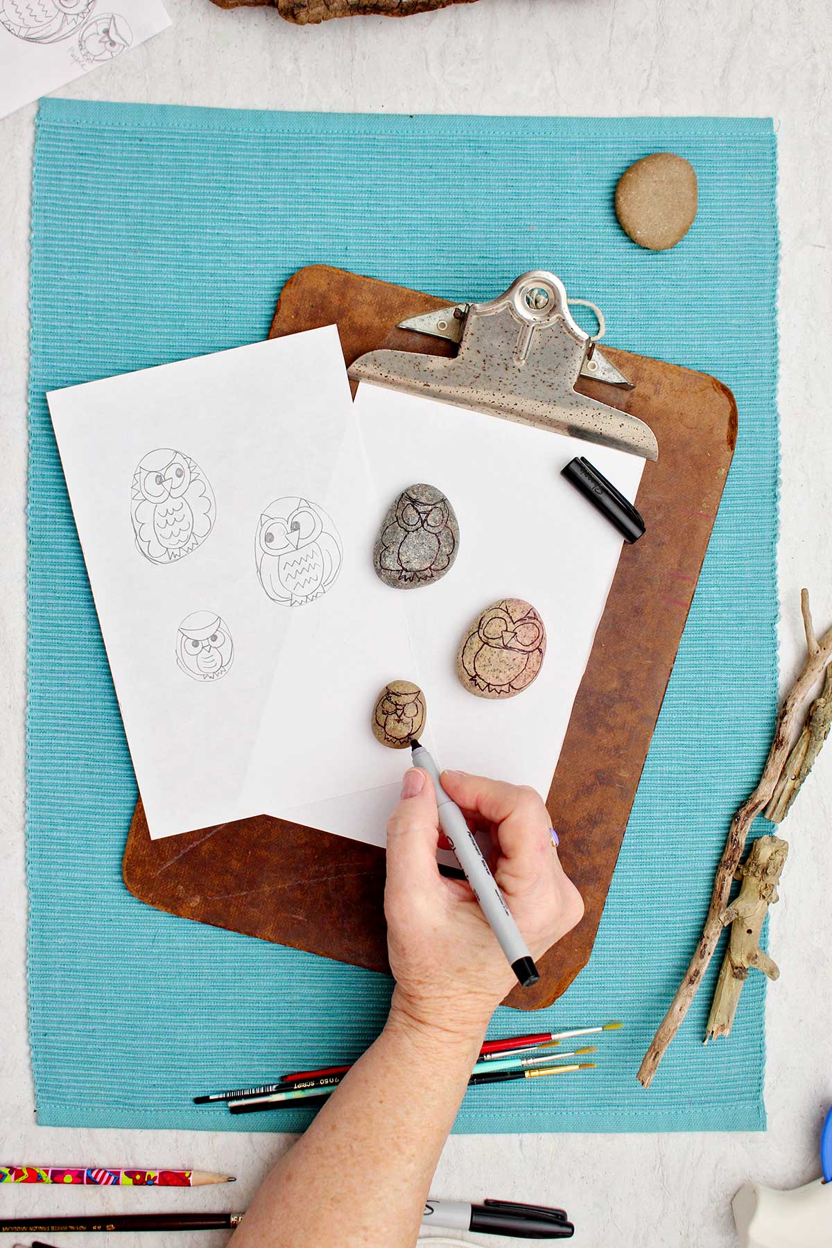 Person using a fine tipped sharpie to draw the outline of an owl on rocks.