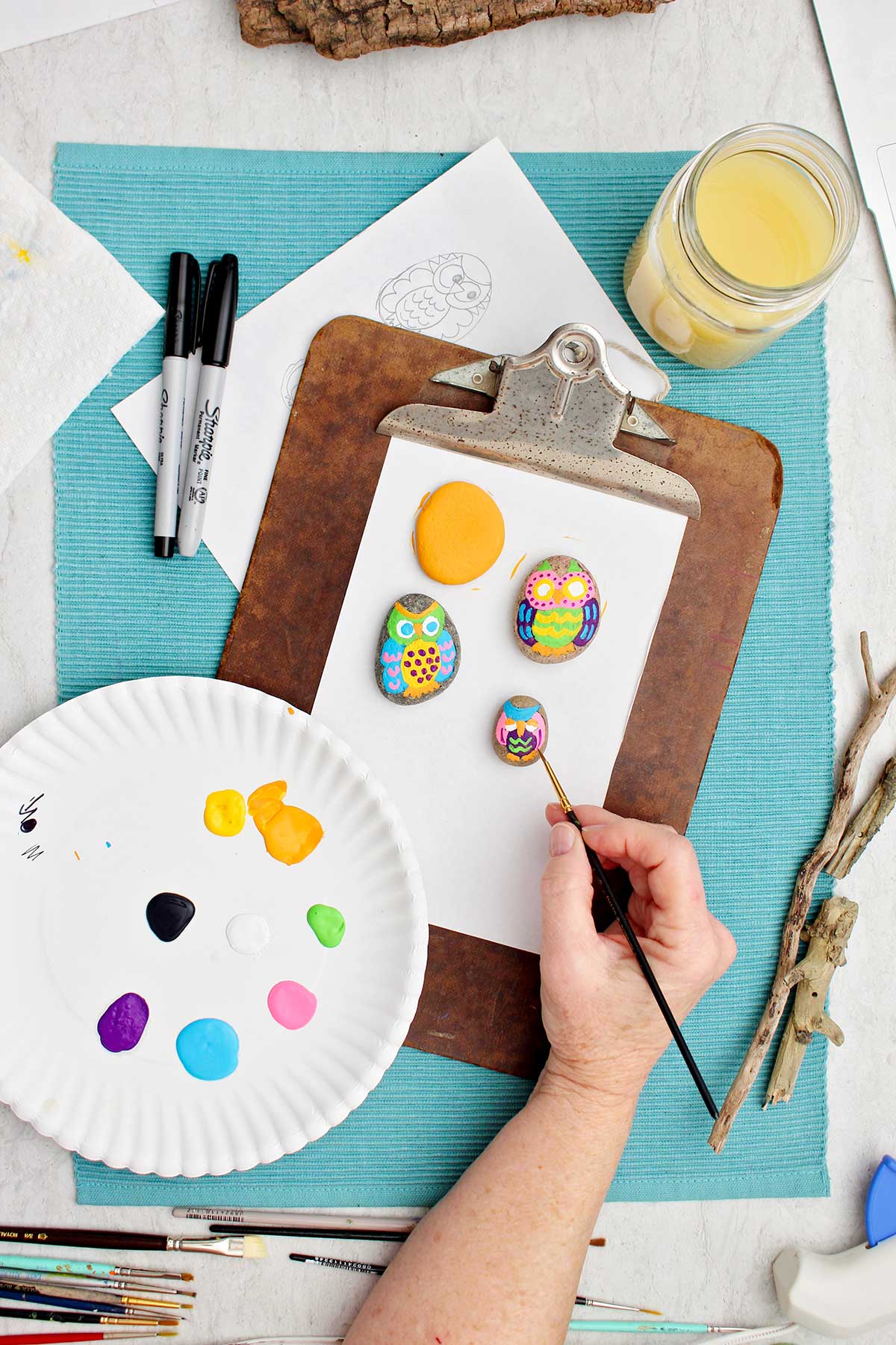 Person painting the smallest owl rock with a fine paintbrush.