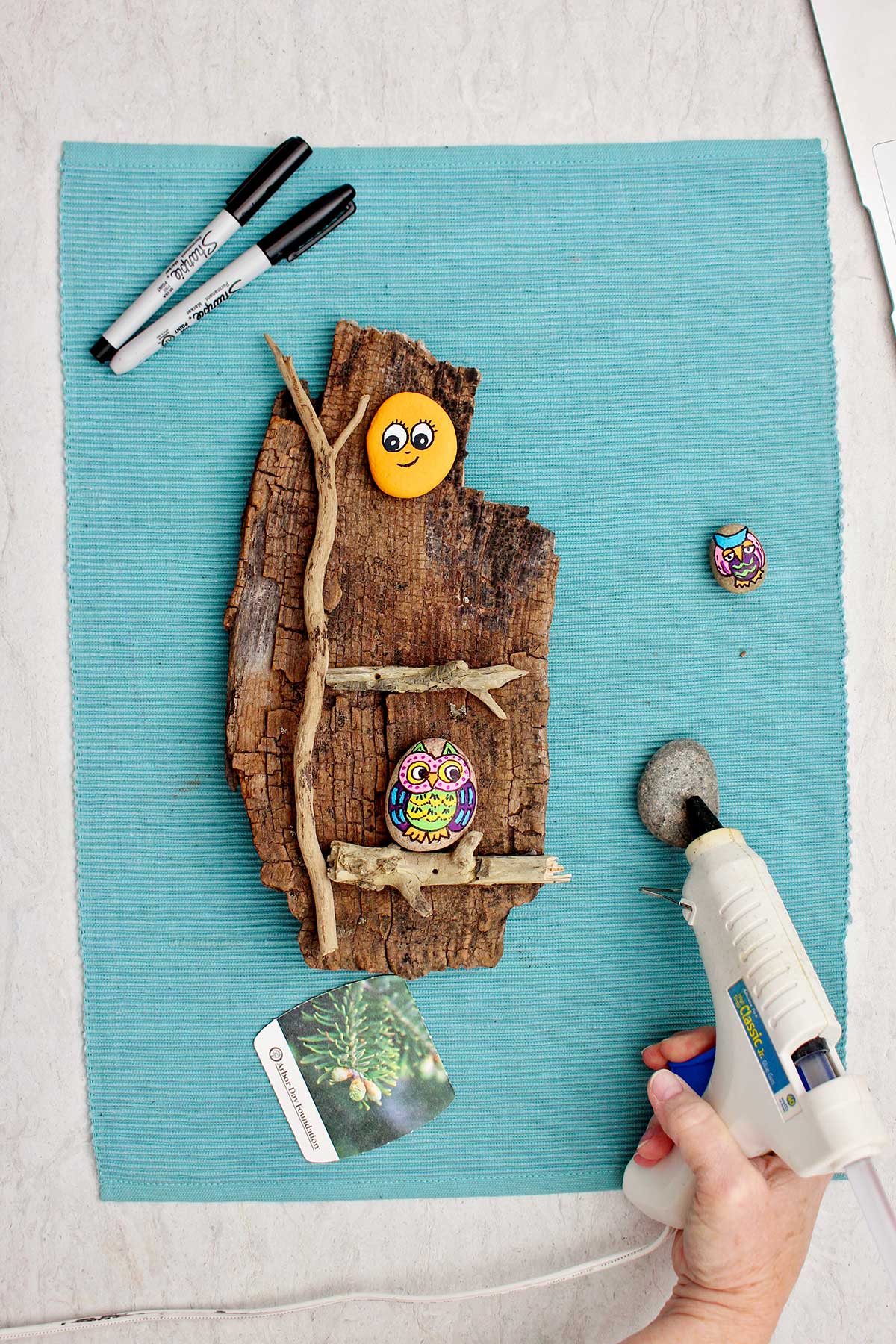 Person hot gluing the back of a painted rock to attach to a piece of wood.